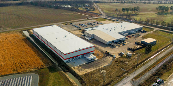 a large warehouse building with trucks parked in a field