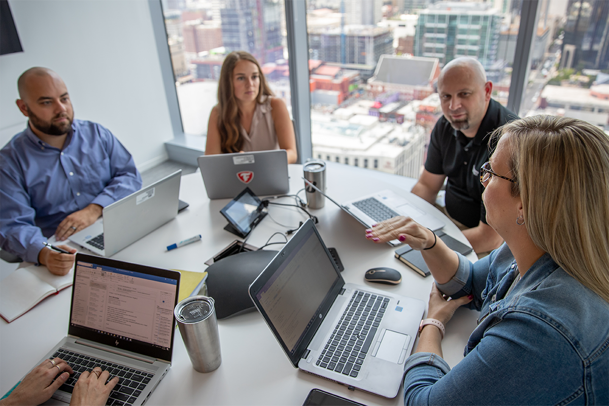 a group of people sitting around a table with laptops