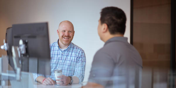 a man sitting at a table with another man in the background