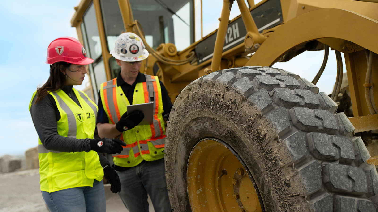 a man and woman in safety vests looking at a large tire