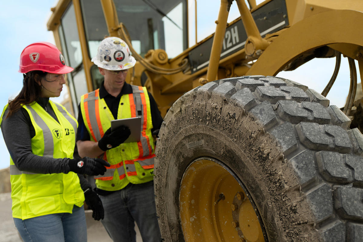 a man and woman in safety vests looking at a large tire
